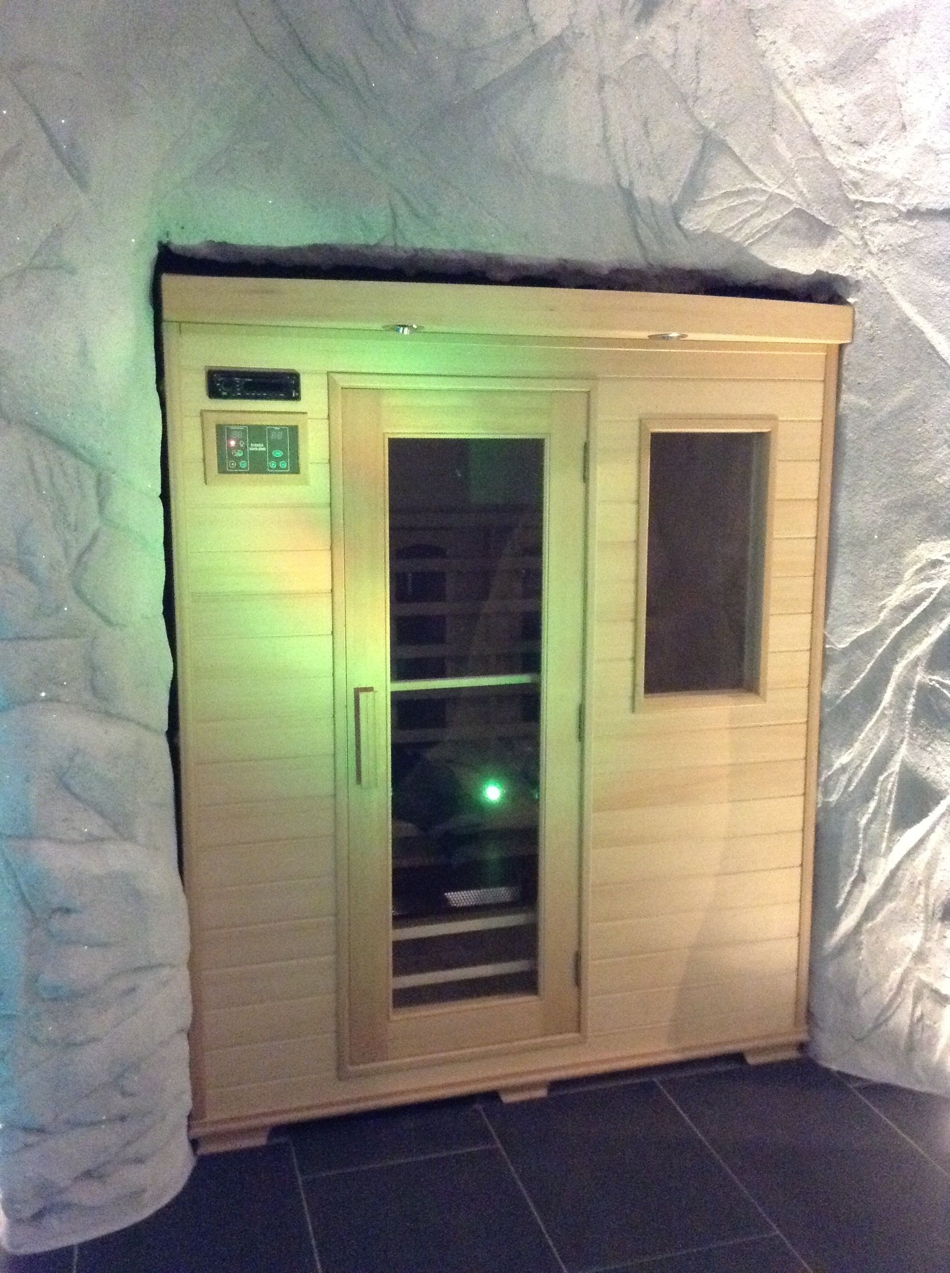 Un sauna avec une structure extérieure en bois, une porte en verre et un panneau de commande situé sur le côté gauche.