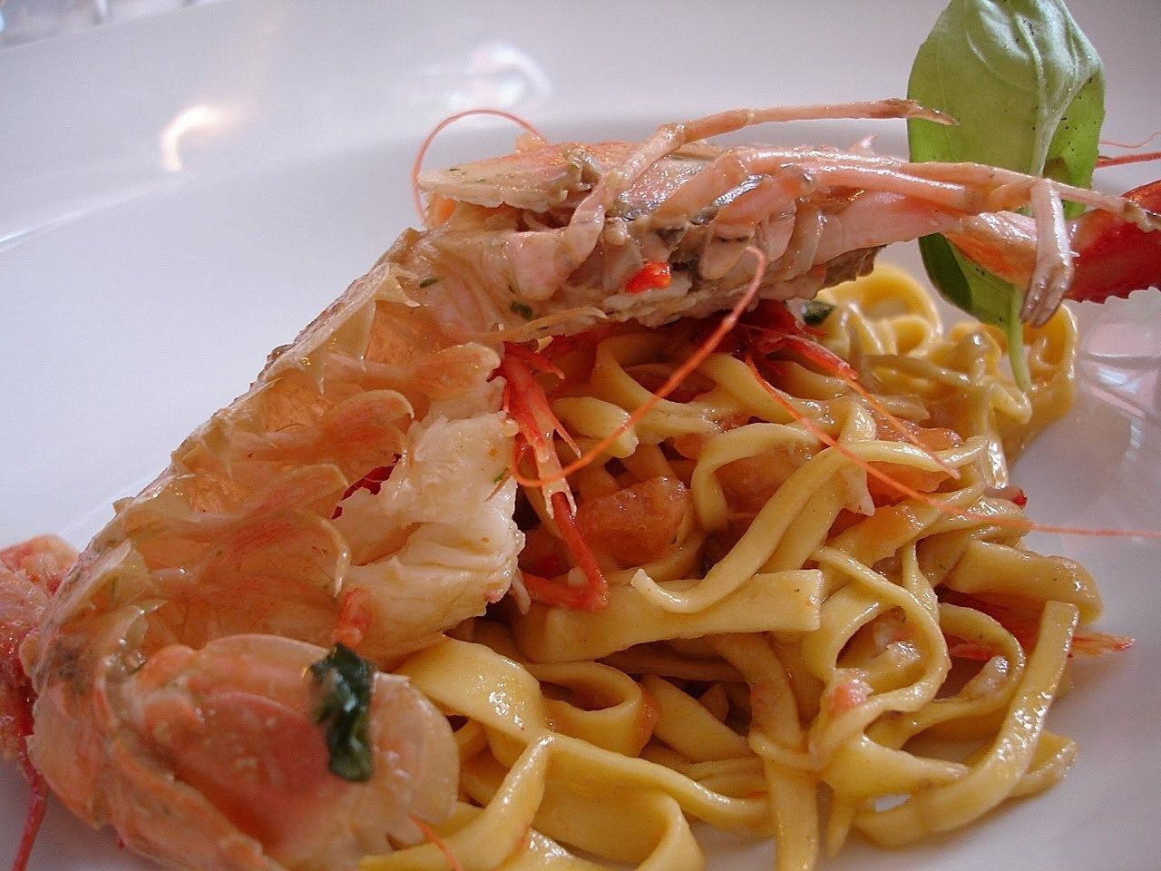 Un piatto di pasta con gamberi e una foglia di basilico.