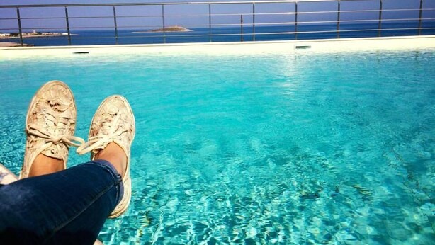 Vista da piscina com água azul cristalina, guarda-corpo metálico e uma ilha ao longe.