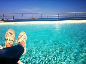 Vista de la piscina con agua azul cristalina, barandilla de metal y una isla distante.