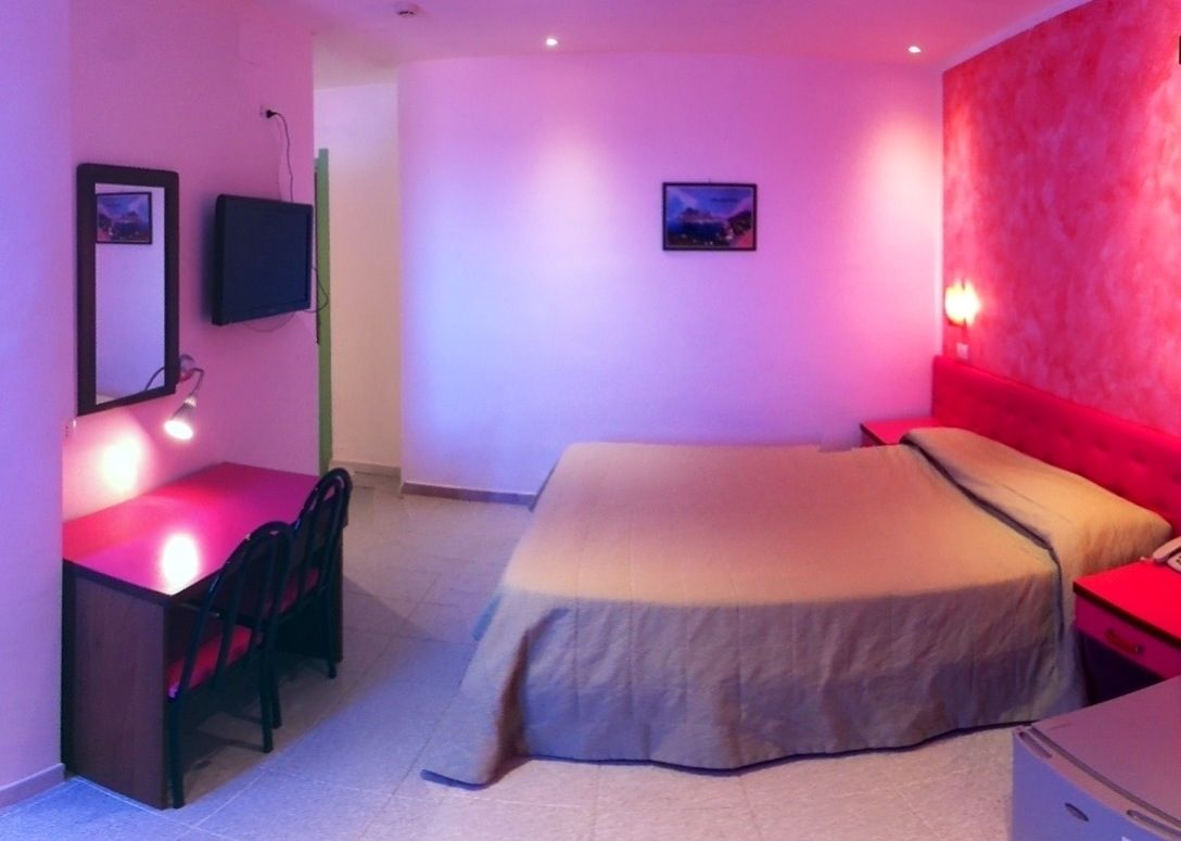 A bedroom with a bed, a desk, and a chair. There is a television mounted on the wall and a picture frame.