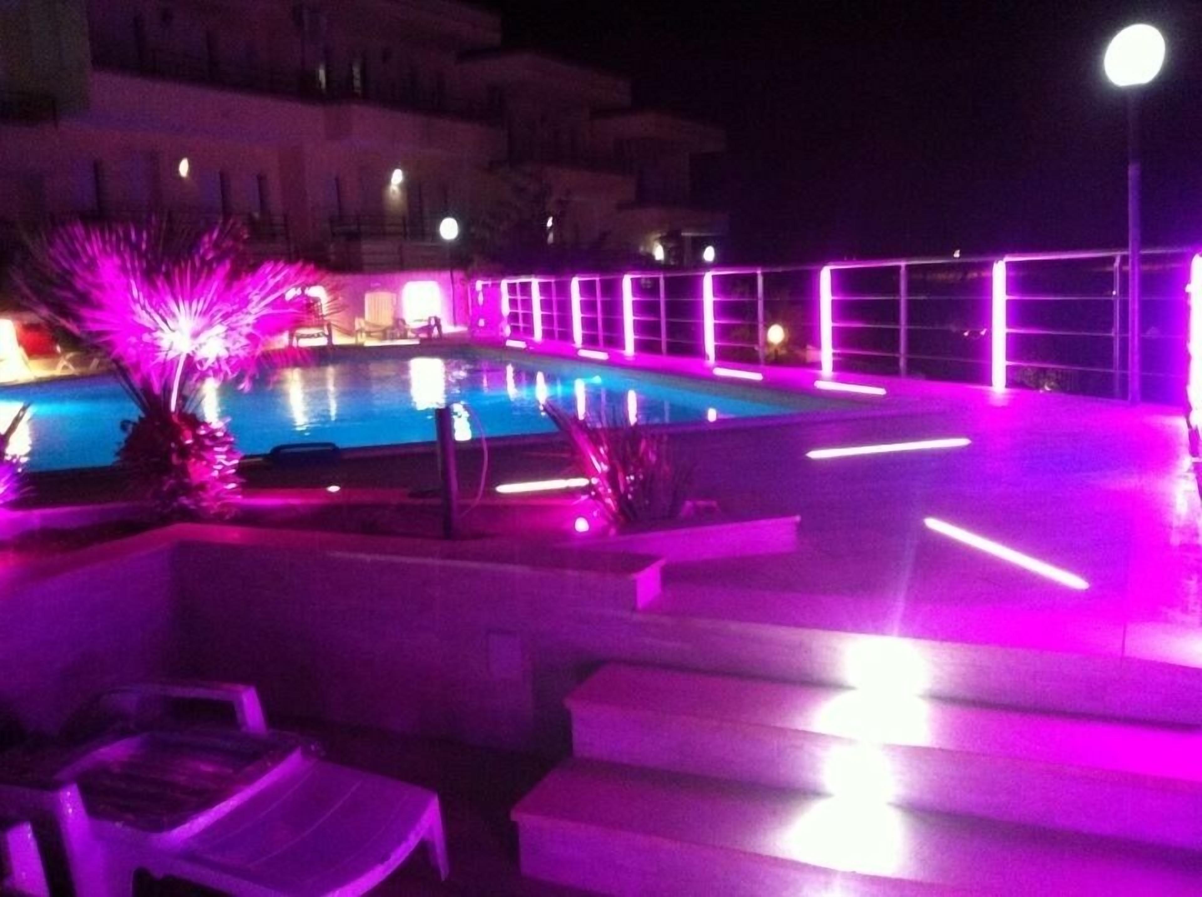 A nighttime pool area with purple lighting, a pool, and lounge chairs.