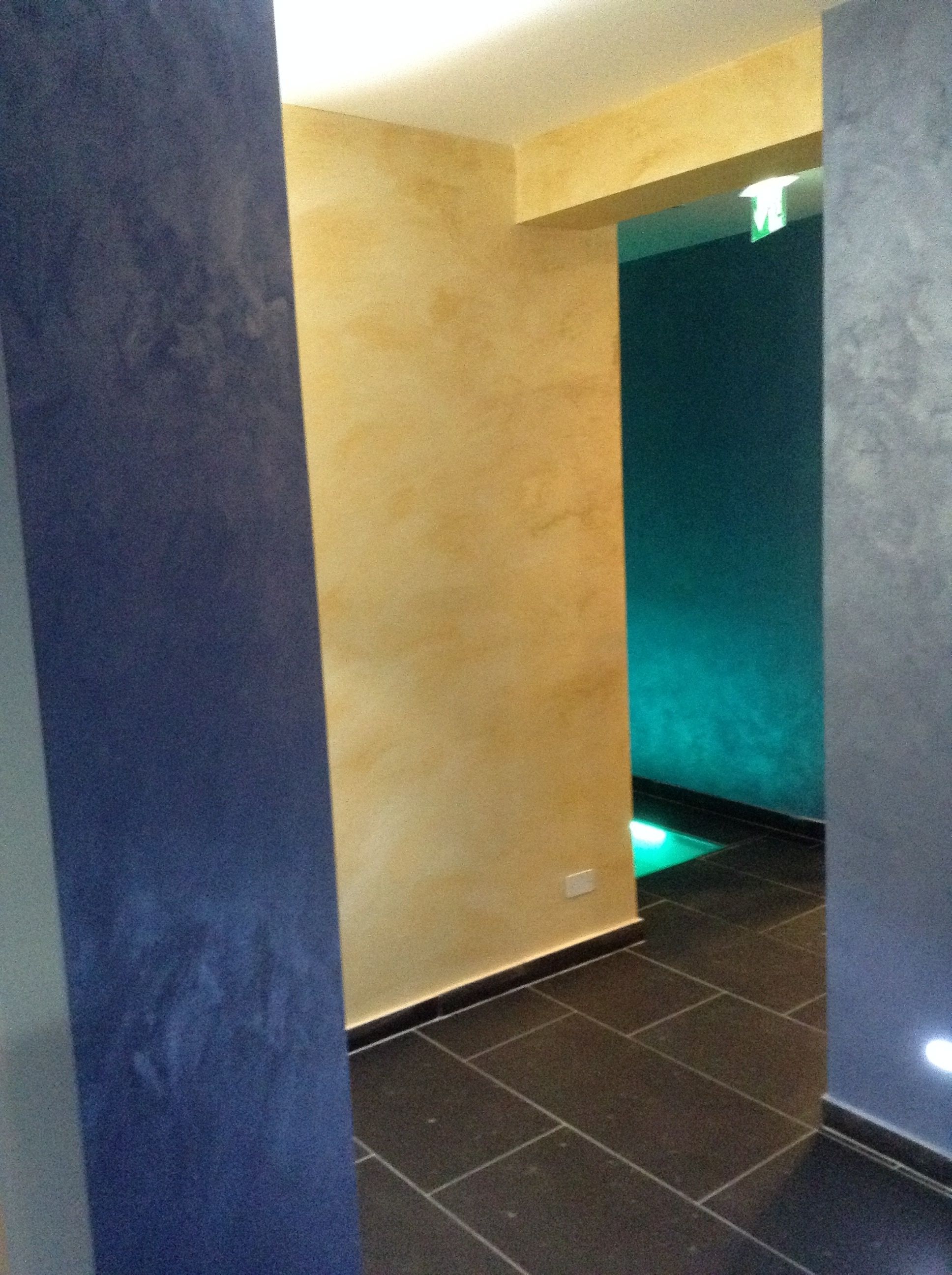A hallway with a blue column, a beige wall, and a teal wall with a light source.
