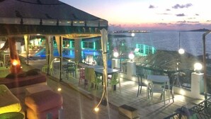 Um restaurante à beira-mar com área externa e vista para o oceano, com um alpendre coberto e zona de piscina.