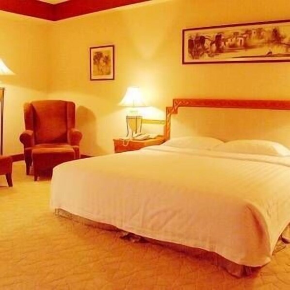Una habitación de hotel con una cama, una silla, una mesita de noche con lámpara y un cuadro en la pared.