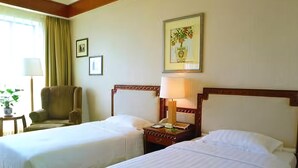 A hotel room with two beds, a chair, a nightstand with a lamp, and framed pictures on the wall.