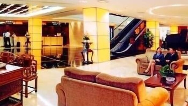 A modern hotel lobby with a reception desk, seating area, and an escalator.