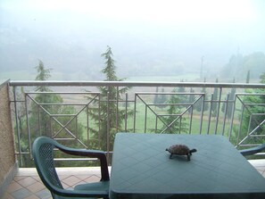 A balcony with a table and a chair, overlooking a misty landscape with trees and a body of water. - Bellavista Country House (Pescara)