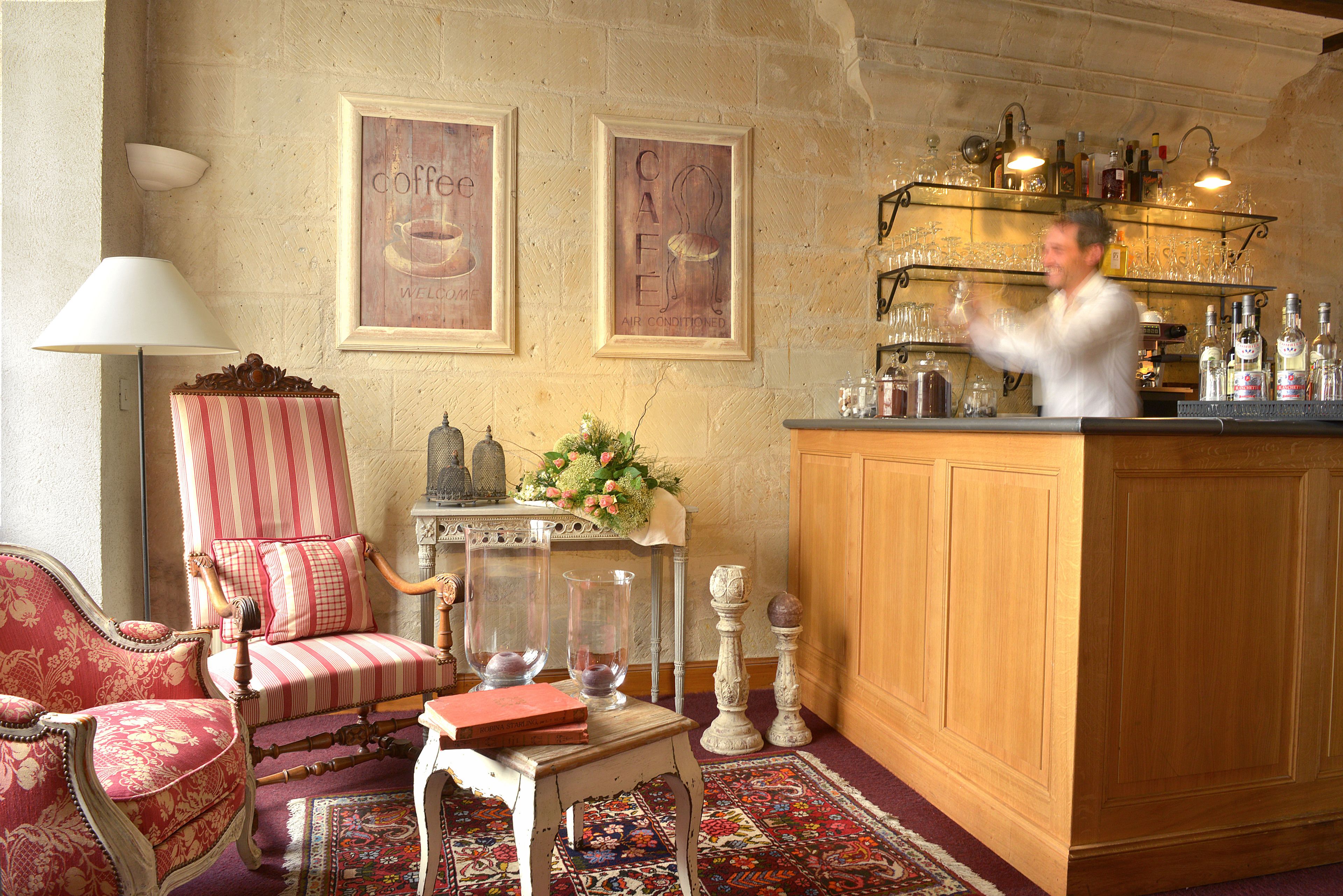 A bar area with a wooden counter, shelves with bottles and glasses, and a decorative chair with a striped cushion.