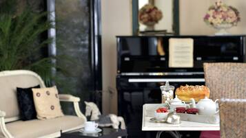 A living room with a piano, a sofa, and a table with tea set and pastries.