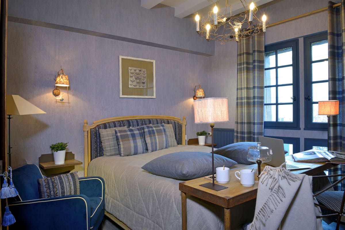 Un dormitorio con cama, mesitas de noche, una silla, escritorio y ventana con cortinas.