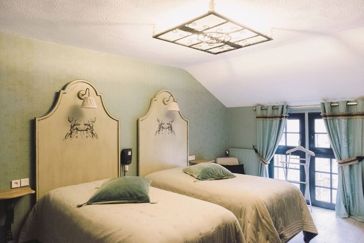 Una habitación con dos camas, una lámpara colgante, un teléfono y una ventana con cortinas.