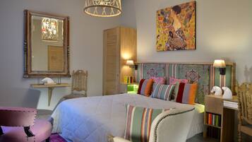 Quarto com uma cama grande, cabeceira de madeira, espelho, lustre, pintura colorida e mesa de cabeceira com livros.