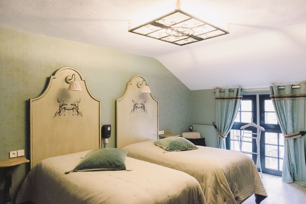 Habitación con dos camas, una lámpara colgante, un radiador y una ventana con cortinas.