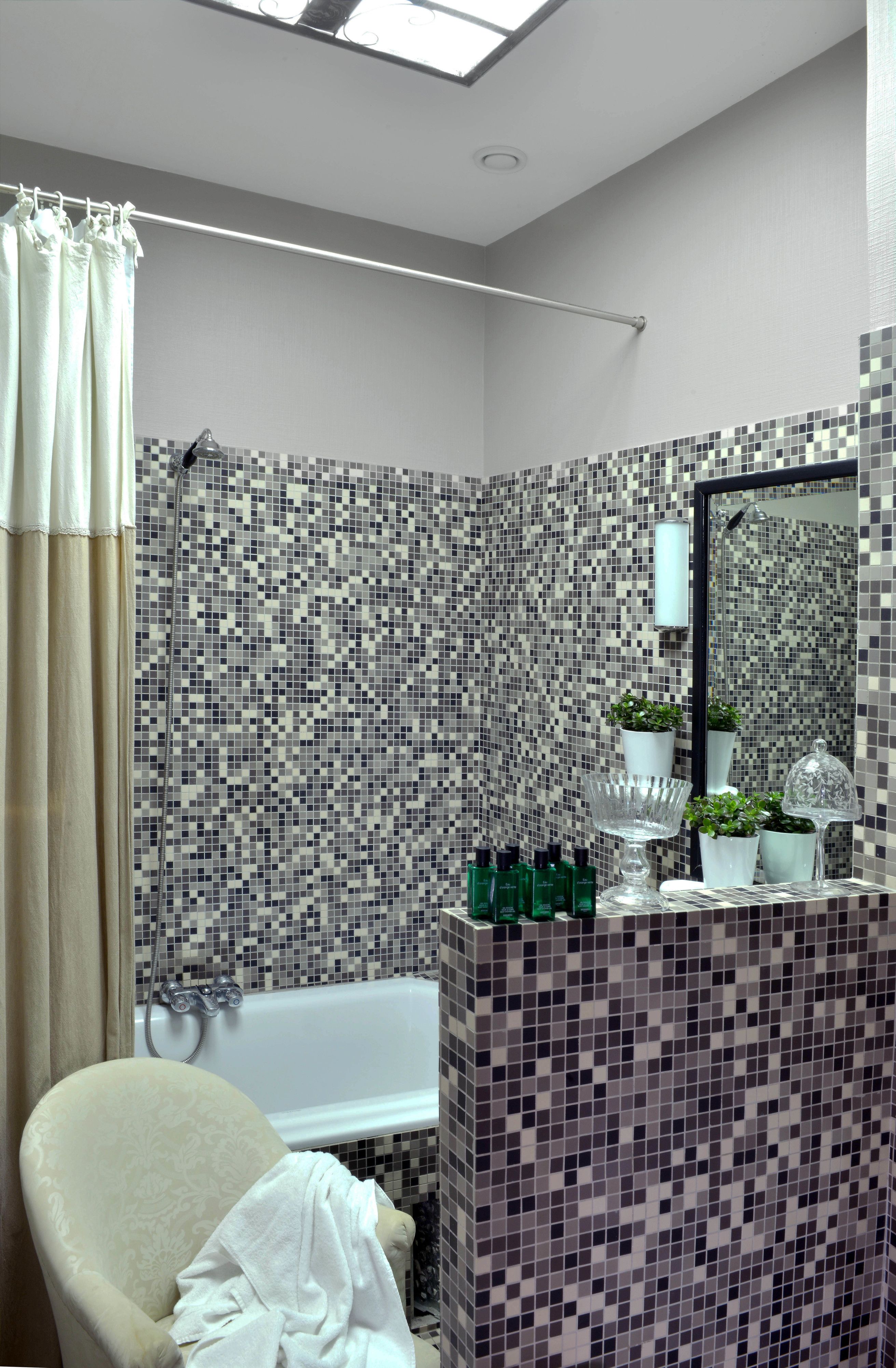 A bathroom with a mosaic tile wall, a bathtub, a shower, a vanity with toiletries, and a mirror.