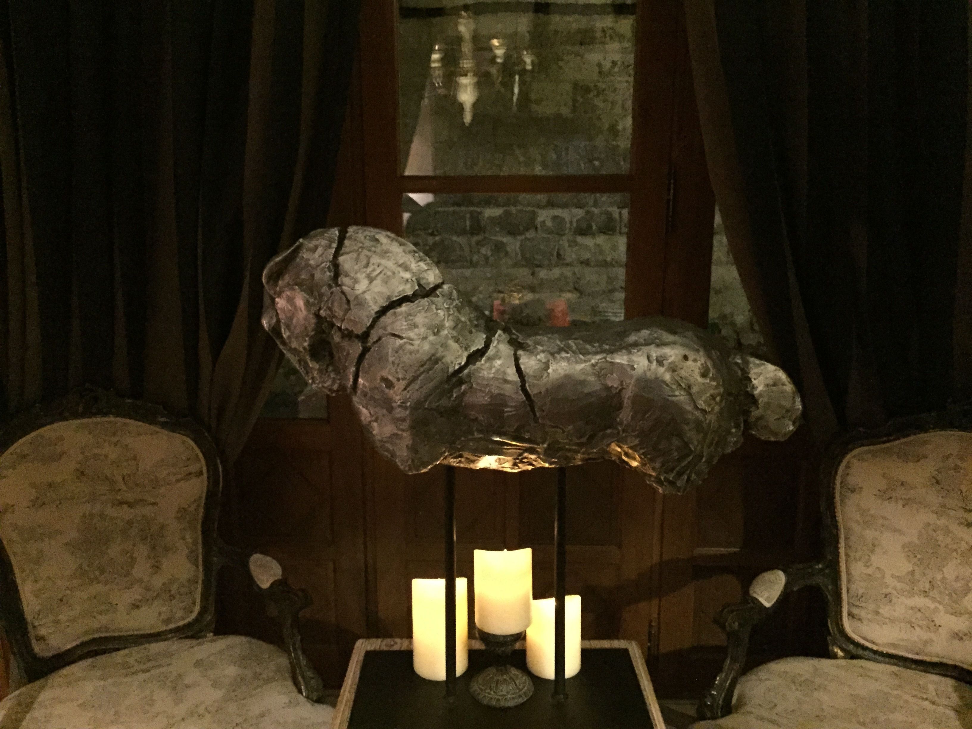 Une sculpture rustique posée sur une table, entourée de bougies, le tout mis en valeur par un mur de pierres et un lambris en bois.