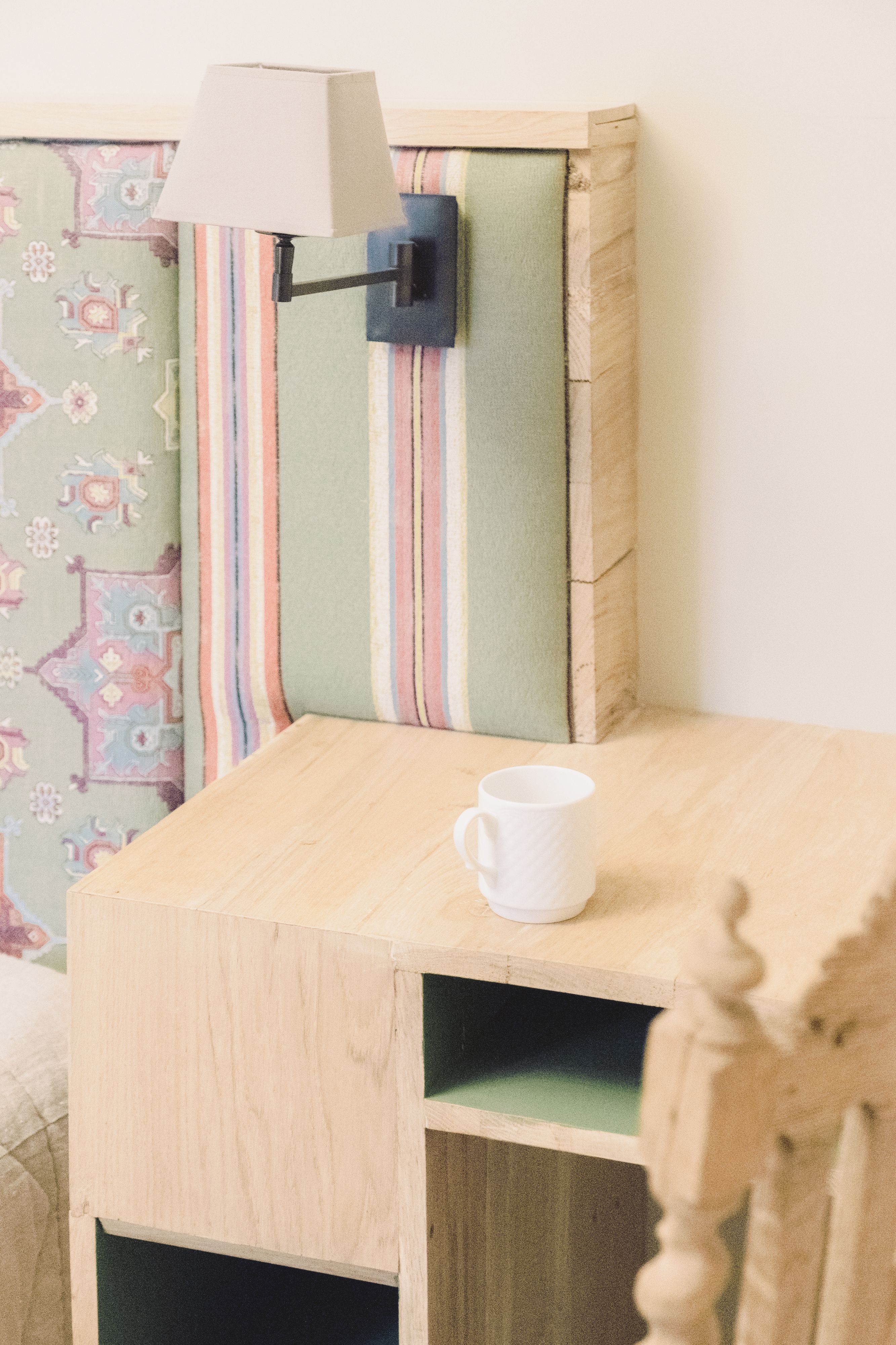 Un coin de pièce avec une table de chevet en bois, une lampe et un coussin à motifs.