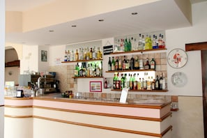 A bar area with shelves of liquor bottles, a clock, and a sign indicating the bar closes at 3:00 AM. - Jolie (Riccione)