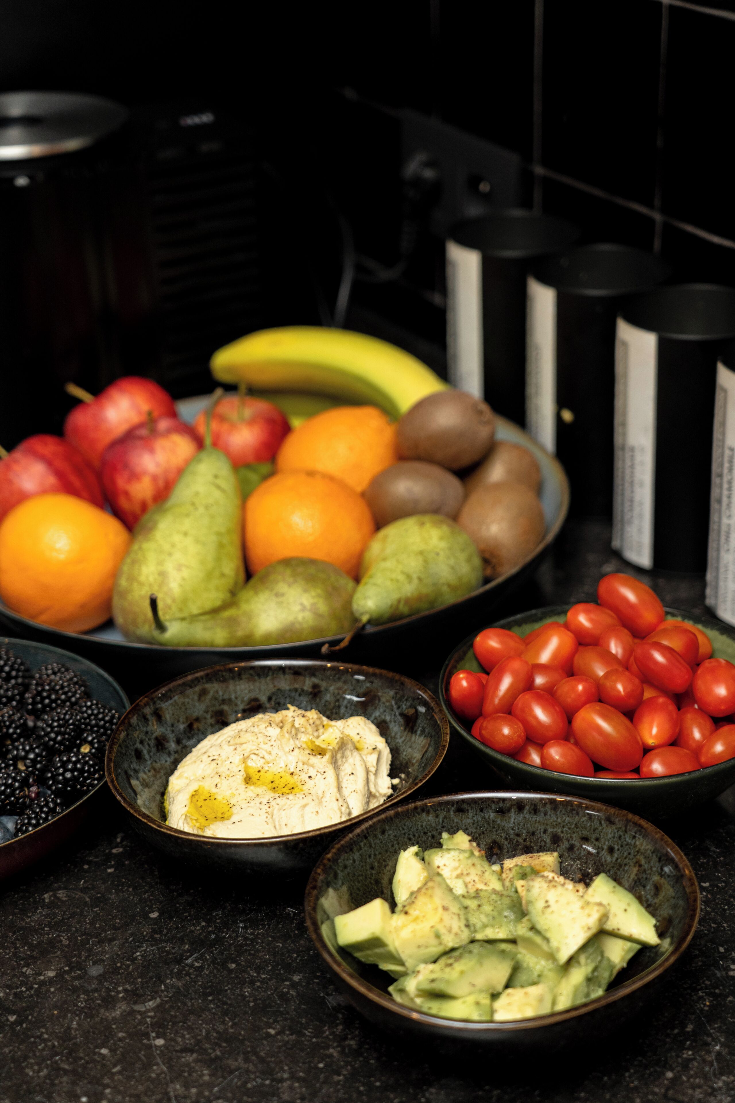 Un piano di lavoro della cucina con diversi tipi di frutta e verdura, tra cui mele, arance, pere, banane e pomodori.