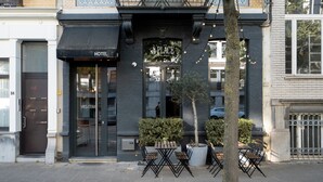 A hotel entrance with a dark facade, a welcoming sign, and outdoor seating. - A Place - Boutique Hotel Emile (Antwerp)