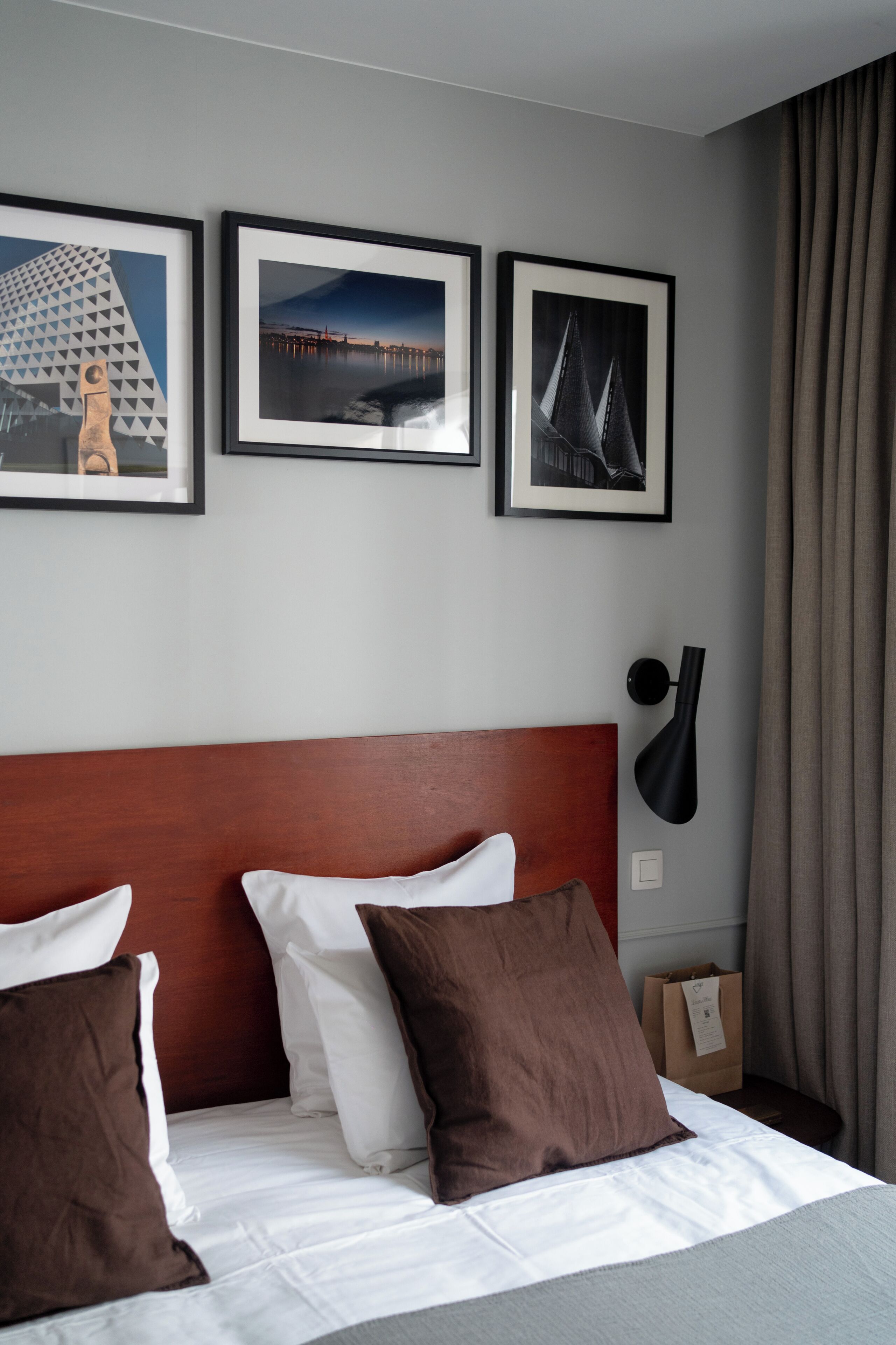 A hotel room with a bed, pillows, a nightstand, a lamp, and framed pictures on the wall.