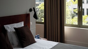 A hotel room with a bed, a nightstand, a lamp, a window with curtains, and framed pictures on the wall. - A Place - Boutique Hotel Emile (Antwerp)