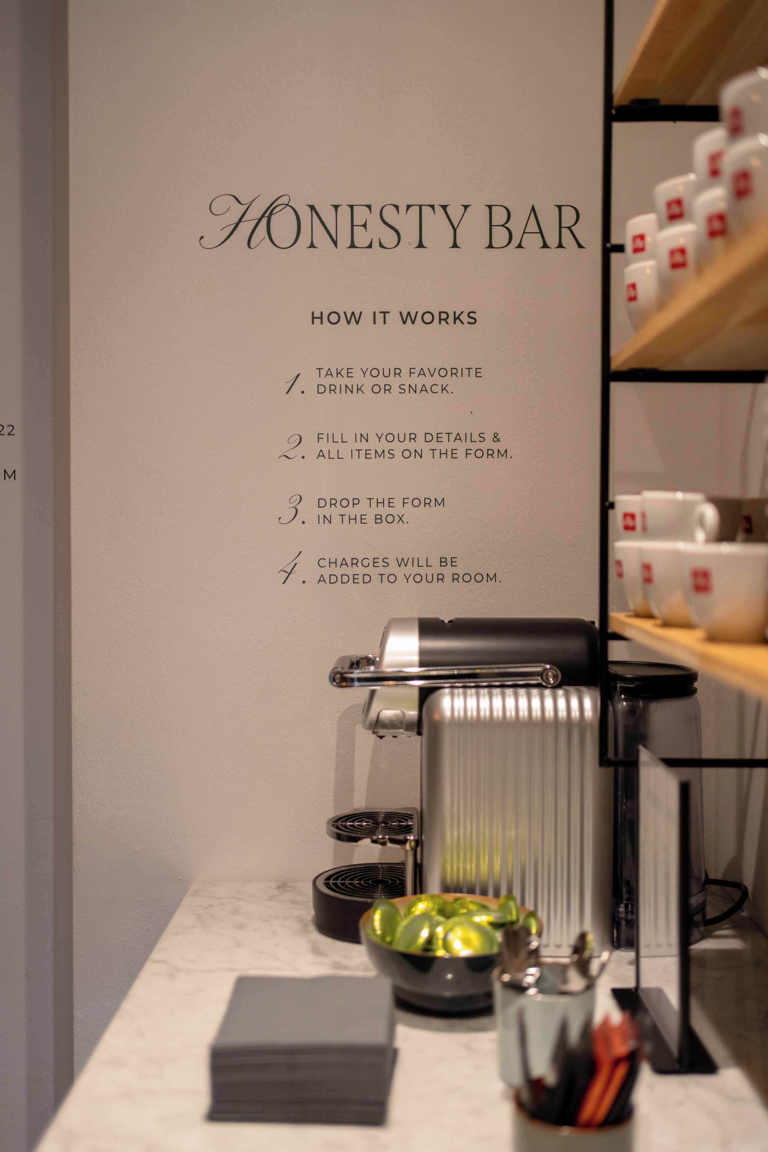 A wall with a list titled 'HOW IT WORKS' for a service, a coffee machine, a bowl of fruit, and a cup holder with utensils.