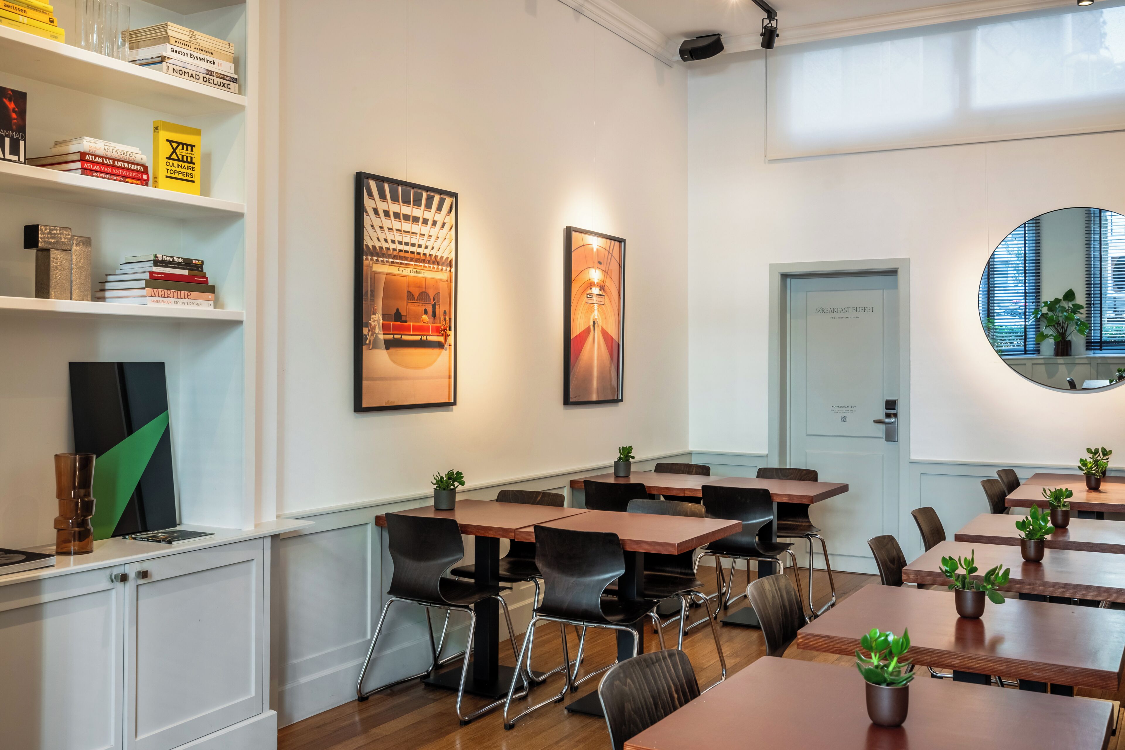 A modern meeting room with white walls, wooden tables, black chairs, and potted plants.