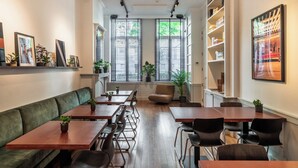 A restaurant with wooden tables and chairs, a green sofa, and a bookshelf. - A Place - Boutique Hotel Emile (Antwerp)
