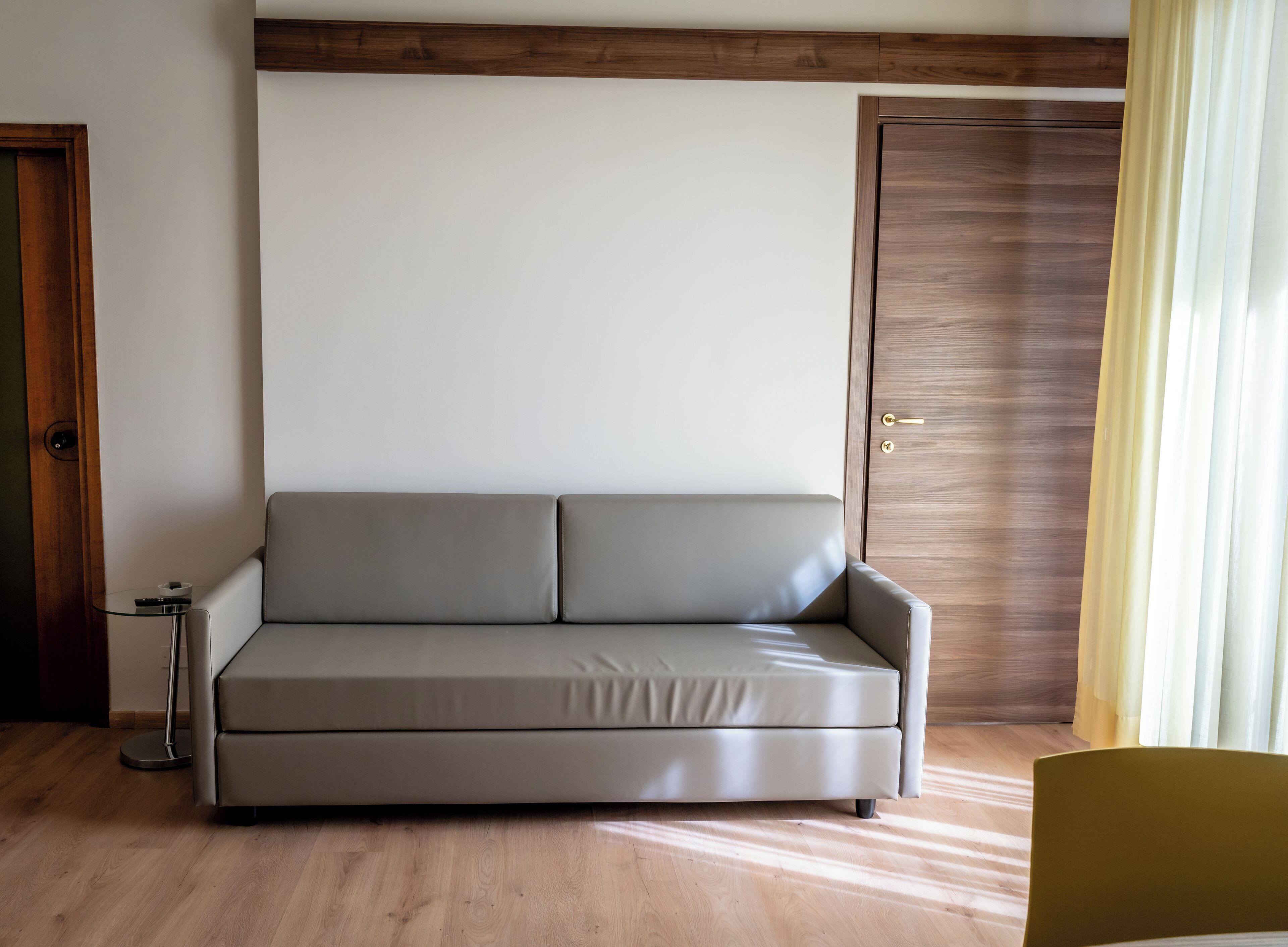 A modern living room with a grey sofa, a wooden door, and a small table with a remote control.