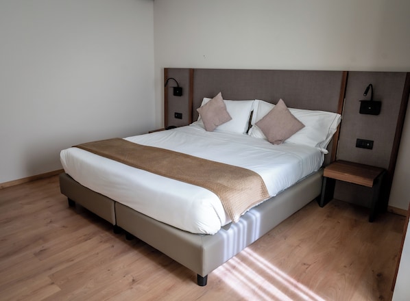 A modern hotel room with a large bed, wooden flooring, and a nightstand with a lamp. - Residence Porta al Prato (Florence)