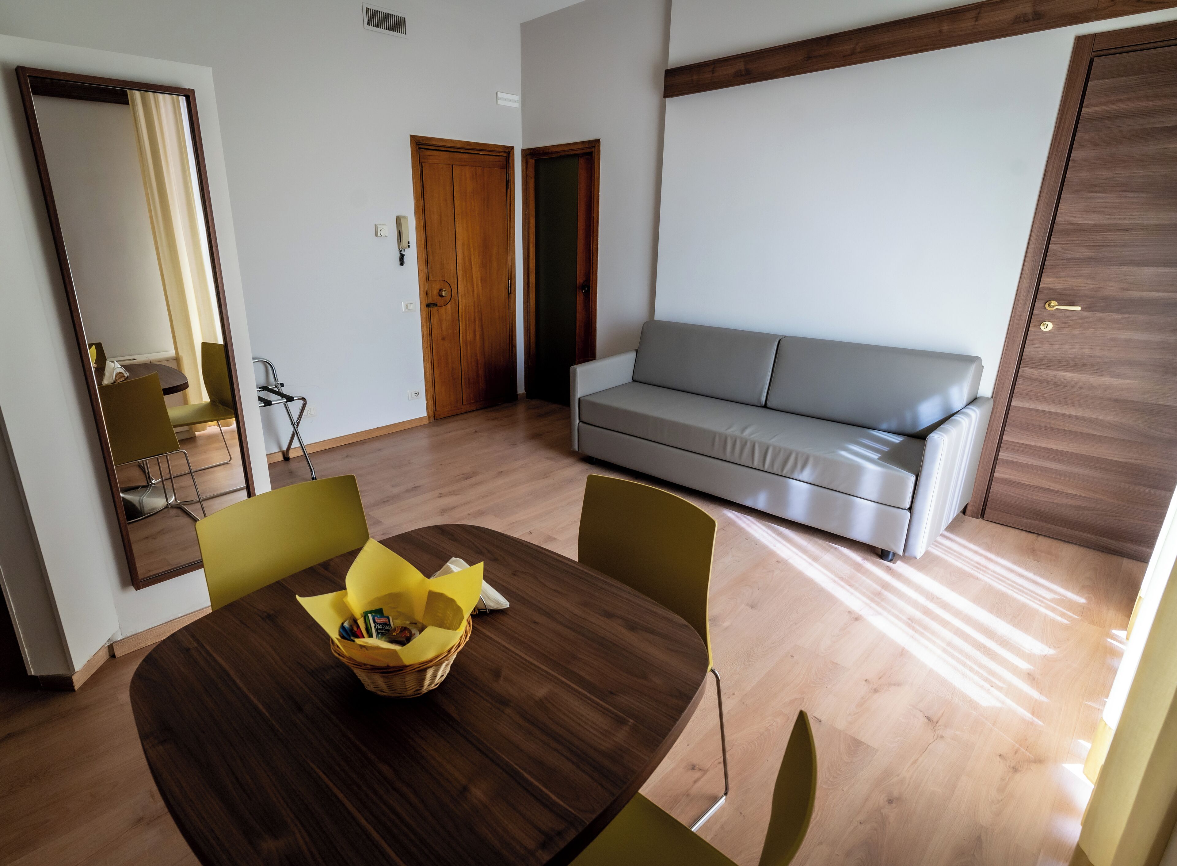 A modern living room with a wooden dining table, a grey sofa, and a yellow chair.