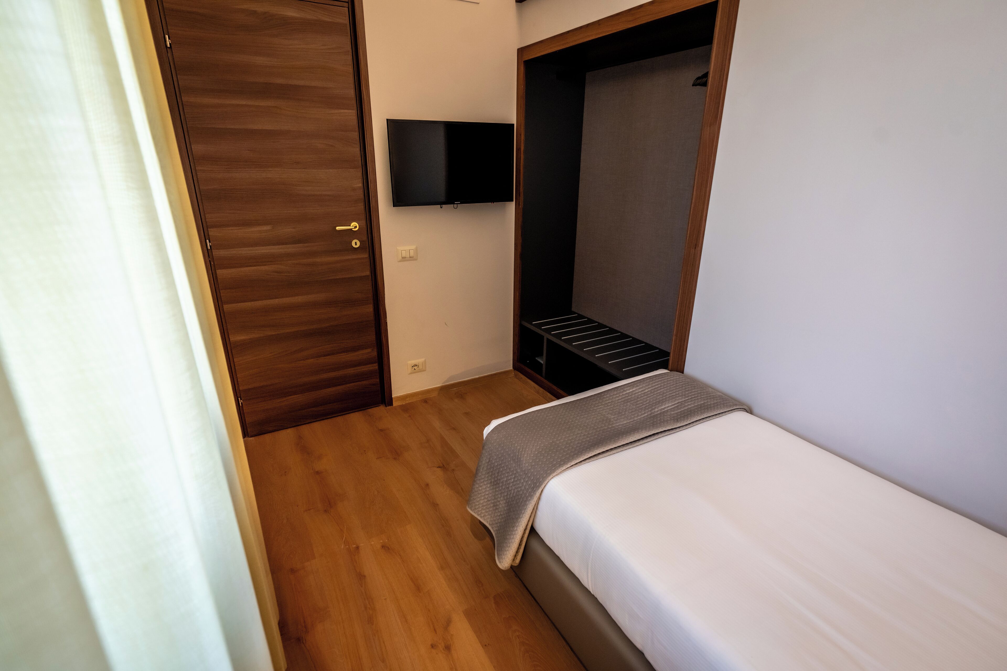 Une chambre à coucher avec un lit, une armoire en bois, un téléviseur fixé au mur et une petite étagère.