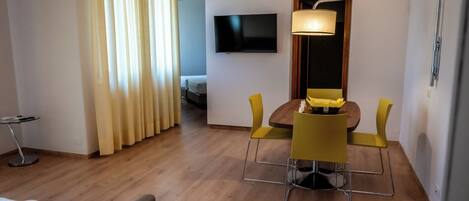A hotel room with a bed, a desk with a chair, a TV mounted on the wall, and a window with curtains.