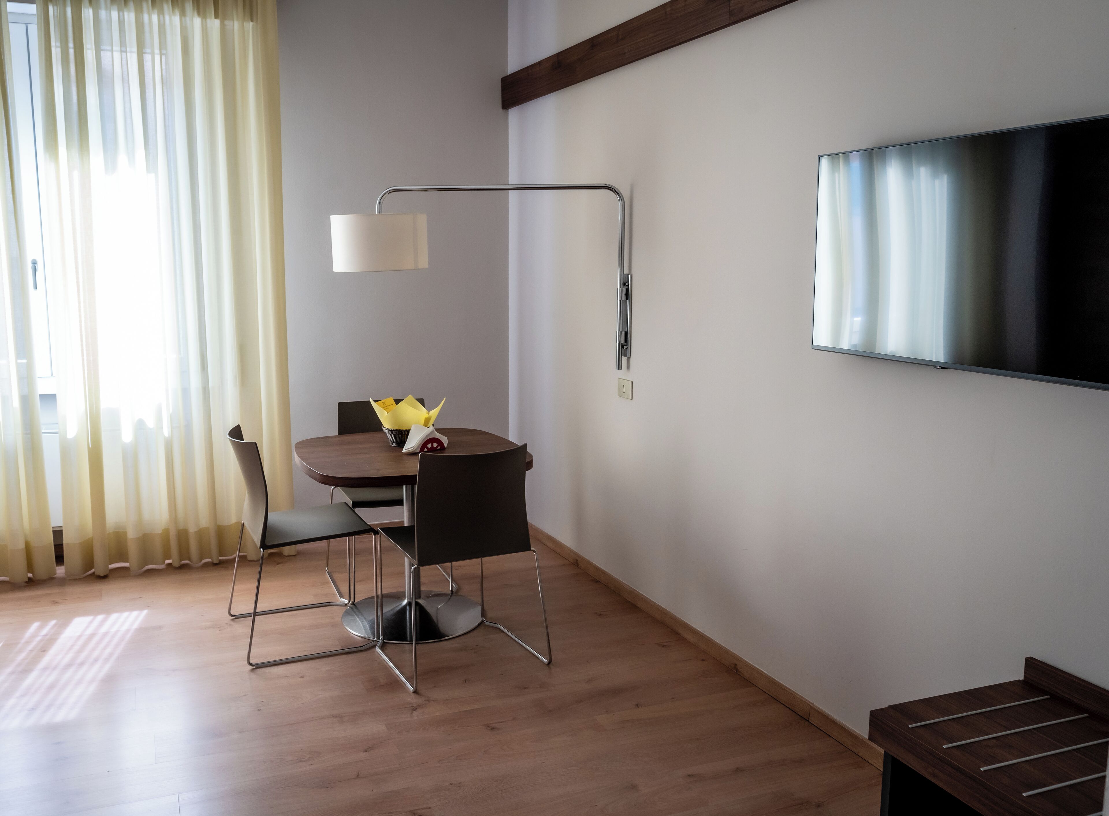 Una habitación moderna con una mesa de comedor, sillas, una lámpara y un televisor de pantalla plana montado en la pared.