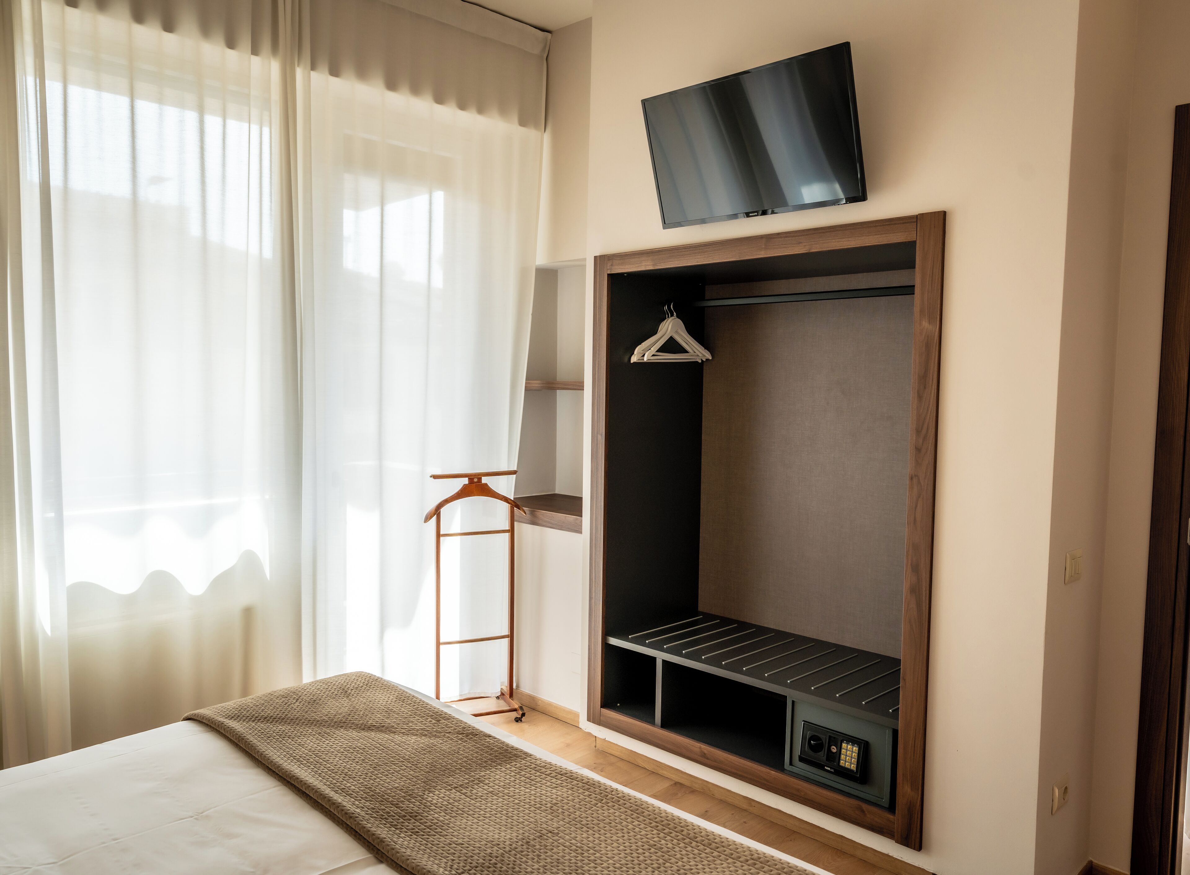 A bedroom with a bed, a TV mounted on the wall, a wardrobe with shelves, and a coat rack.
