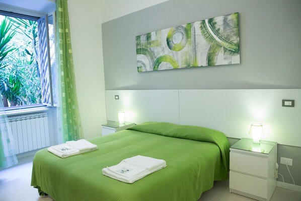 Une chambre d’hôtel avec un lit, une literie verte, une table de chevet avec une lampe et une fenêtre avec des rideaux.