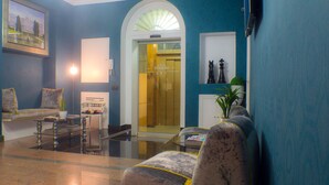 A lobby with a sofa, armchairs, a coffee table, a reception desk, and a door with a sign. - Hostal Oriente (Madrid)