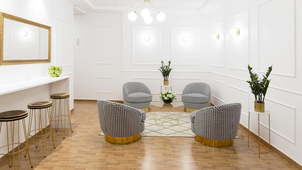 A modern interior with a white color scheme, featuring a central seating area with patterned chairs, a wooden floor, and a decorative chandelier. - Hostal Oriente (Madrid)