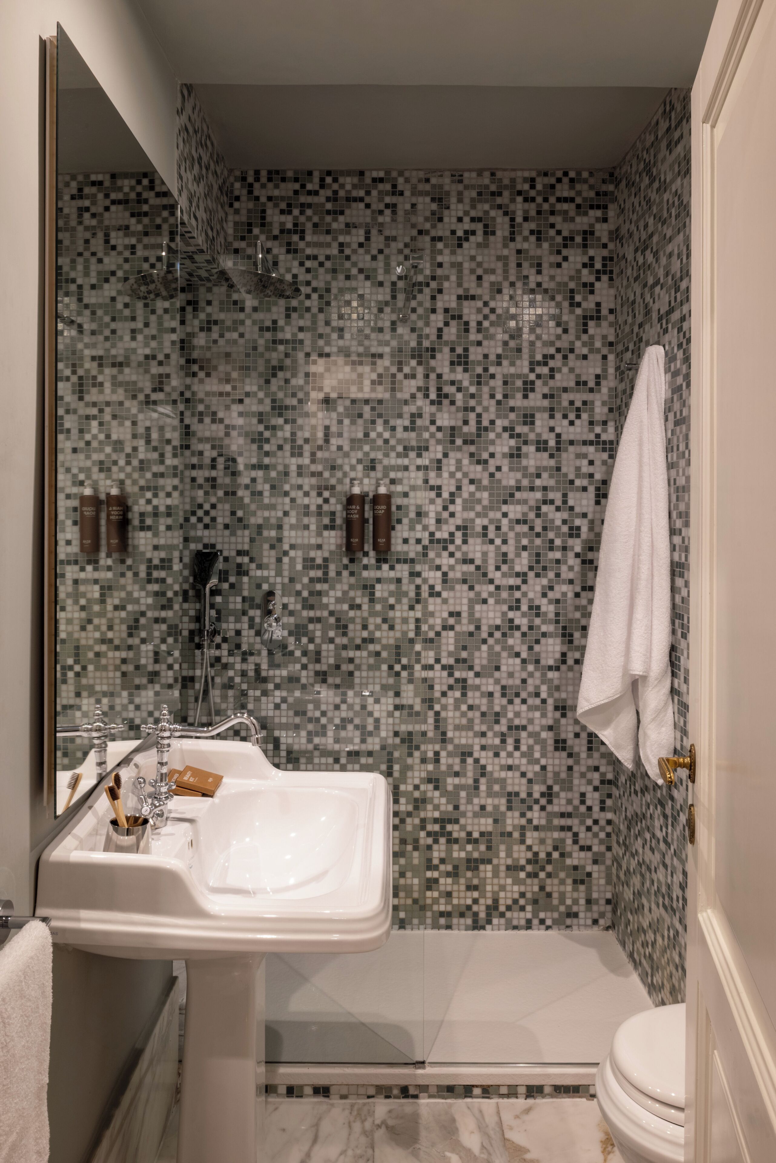 Un baño con pared de ducha de mosaico, un lavamanos blanco y un inodoro.