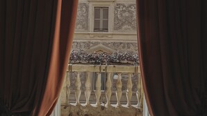 A view through a window with curtains, revealing a balcony with a balustrade and a building with ornate architectural details. - Hotel City Palazzo dei Cardinali (Rome)