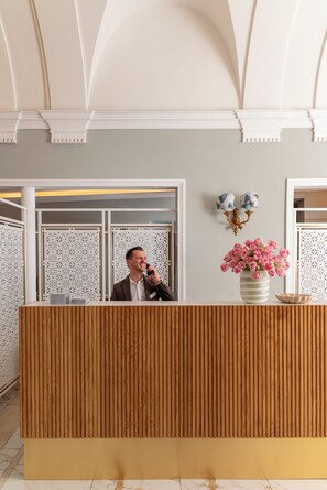 Un comptoir d’accueil avec un homme au téléphone, un vase de fleurs et des appliques murales décoratives.