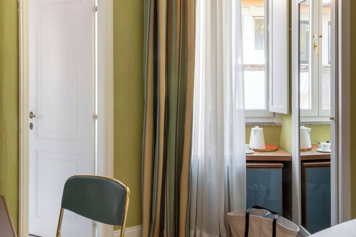 Ein Hotelzimmer mit Holzboden, einem Sessel, einem Bett, einem Schreibtisch mit Lampe und einem fenster mit Vorhängen.