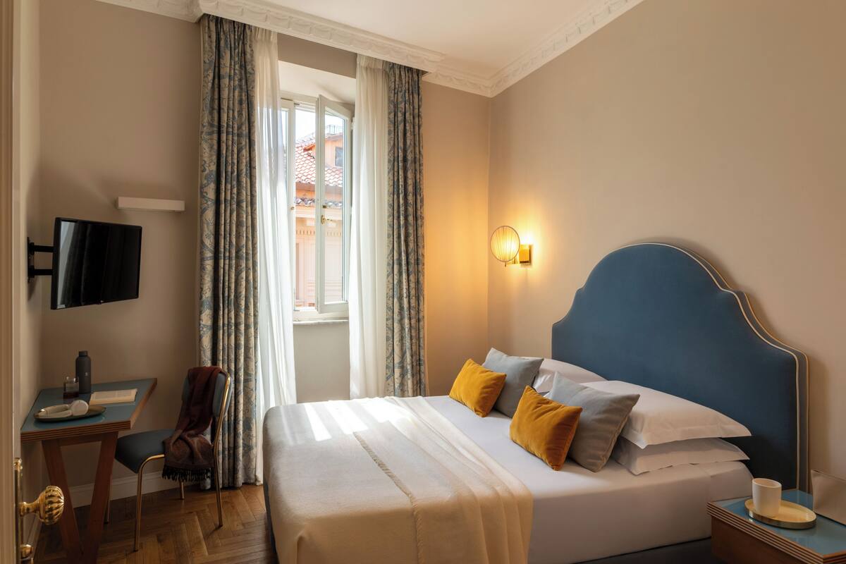 Ein Hotelzimmer mit Bett, Schreibtisch, Stuhl, Fernseher und einem fensterbepflanzten Fenster.