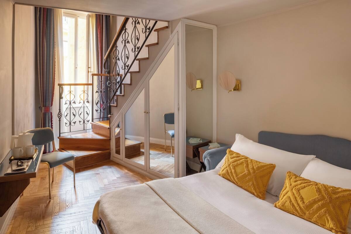 Ein Hotelzimmer mit Bett, Schreibtisch, Stuhl, einer Treppe und Blick ins Freie.