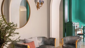 A modern living room with a grey sofa, matching armchairs, a gold coffee table, and a large mirror. - Hotel City Palazzo dei Cardinali (Rome)