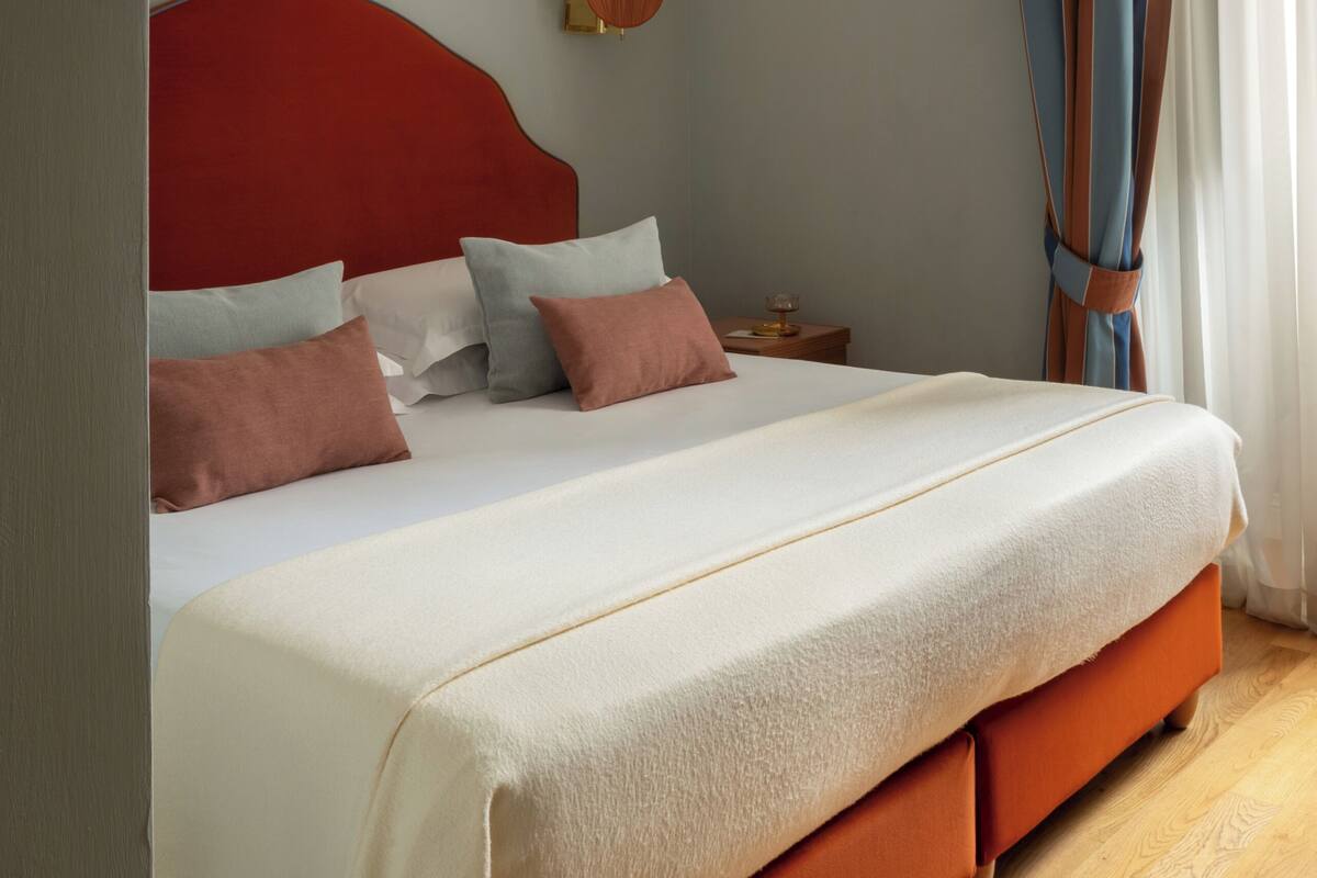 Ein Schlafzimmer mit einem großen Bett, einem Nachttisch, einem Wandventilator und einem Fenster mit Vorhängen.