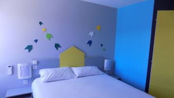 Una habitación de hotel con cama, mesita de noche, lámpara de pared y puerta.