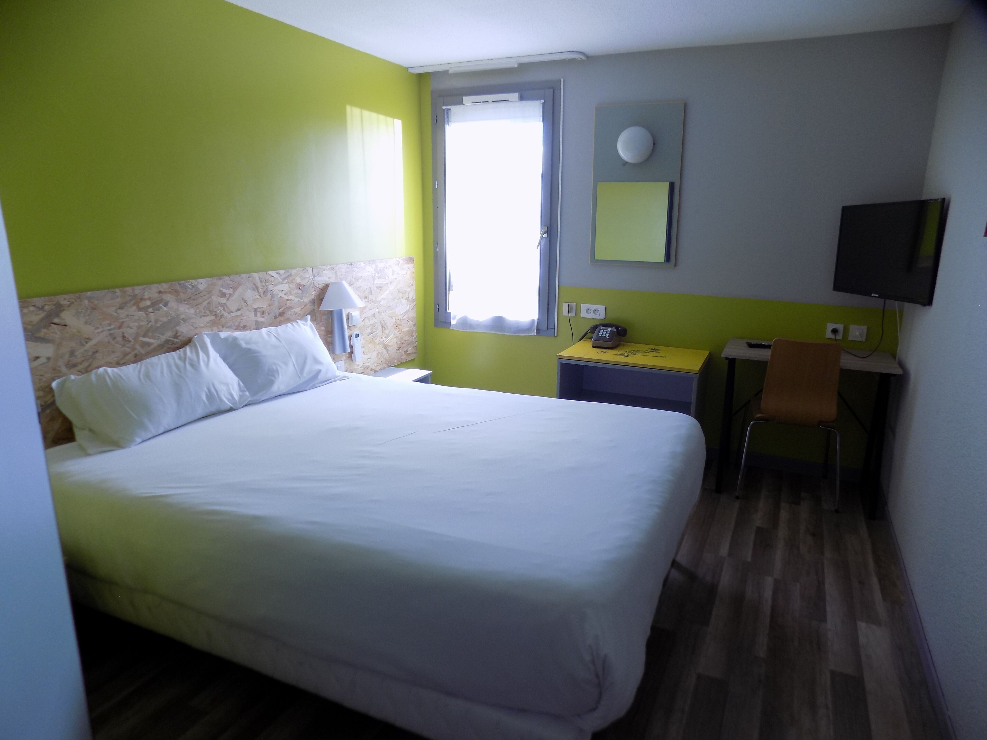 Una habitación de hotel con cama, escritorio, silla, televisor y ventana.