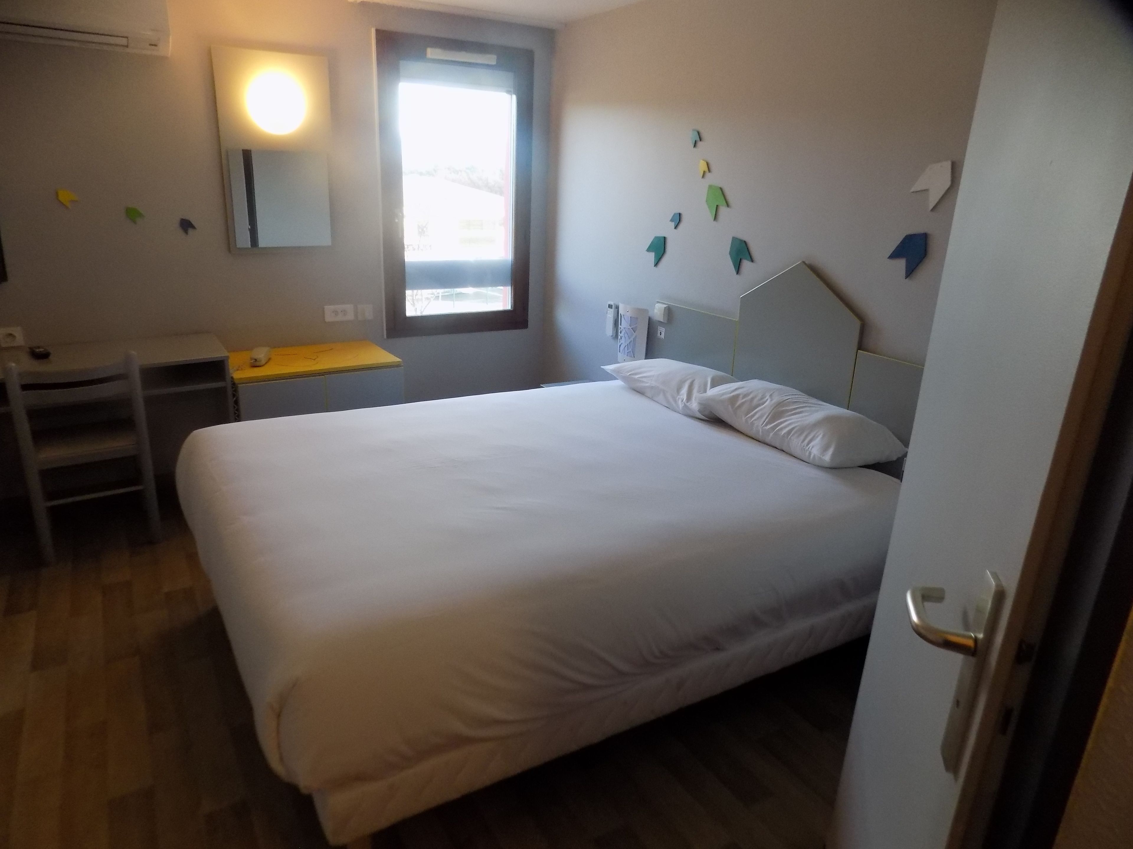 Un dormitorio con cama, escritorio y silla. Se ve un ventanal con vistas al exterior.